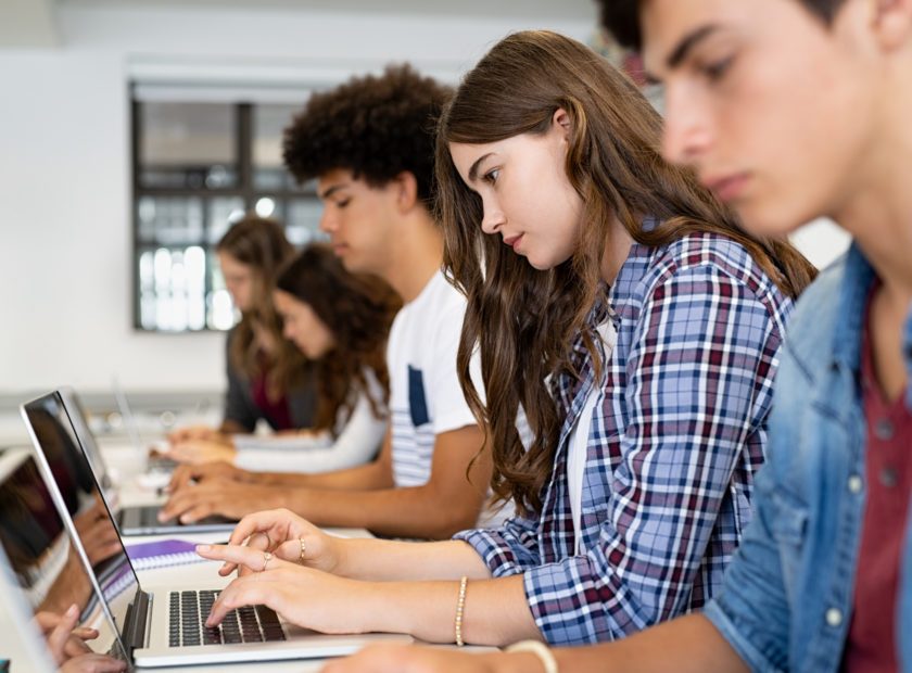 Group of high school students using laptop in classroom