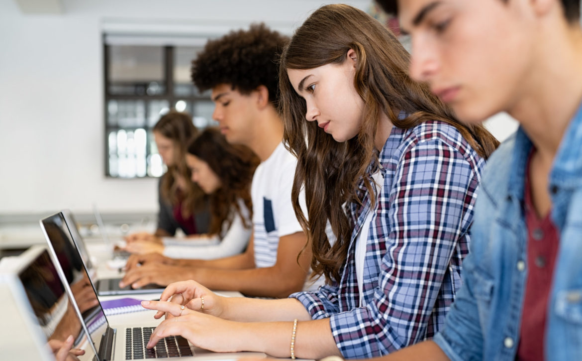 Group of high school students using laptop in classroom